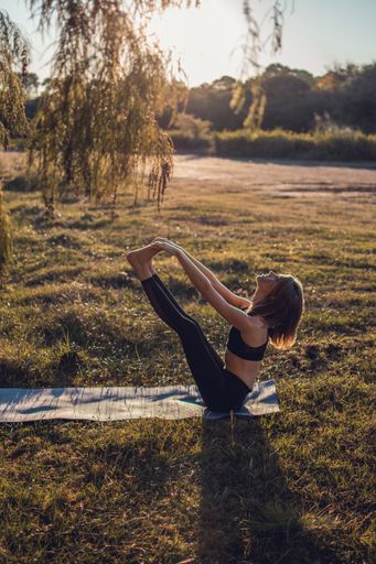 A vertical shot of a young female doing yoga on a mat in a field under the sunlight