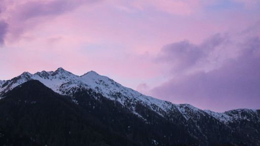A beautiful view of a mountain range covered in snow against a pink cloudy sky