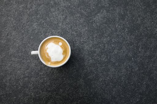 A top view of a cup of cappuccino coffee on a concrete surface