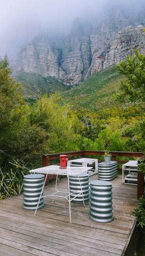 A vertical shot of a wooden balcony with spring-shaped chairs and a coffee table in the middle of green mountains
