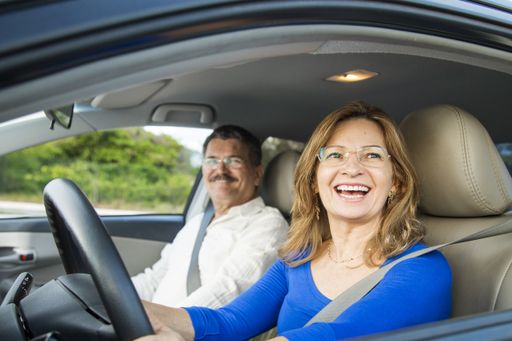 A closeup shot of a middle-aged Hispanic couple wearing glasses smiling in a car with the wife driving