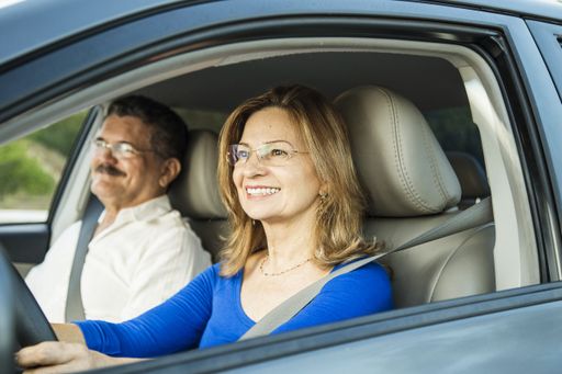 A closeup shot of a middle-aged Hispanic couple wearing glasses smiling in a car with the wife driving