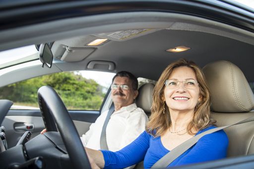 A closeup shot of a middle-aged Hispanic couple wearing glasses smiling in a car with the wife driving