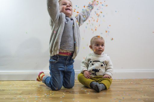 A 4-year-old Caucasian girl throwing confetti in the air while sitting on the floor next to her cute toddler sister