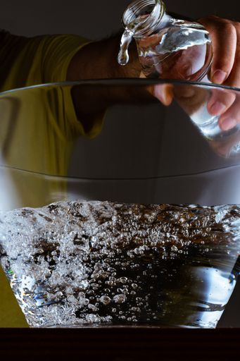 A closeup of a male pouring clean water into a glass bowl