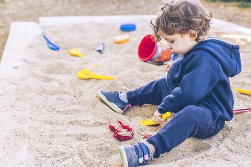 A closeup shot of a boy playing with sand in the playground at daytime