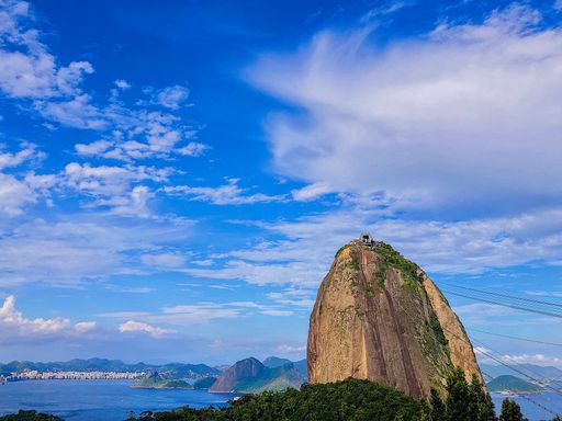 A scenic view of Sugarloaf Mountain against a blue cloudy sky in Rio de Janeiro, Brazil
