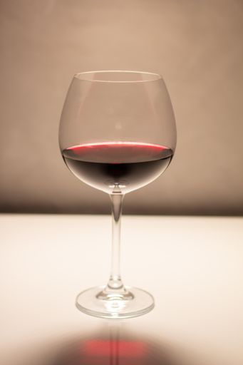 A vertical closeup of red wine in a glass on a white reflective surface