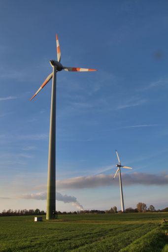 A vertical low angle of wind turbines in the field against blue sky background