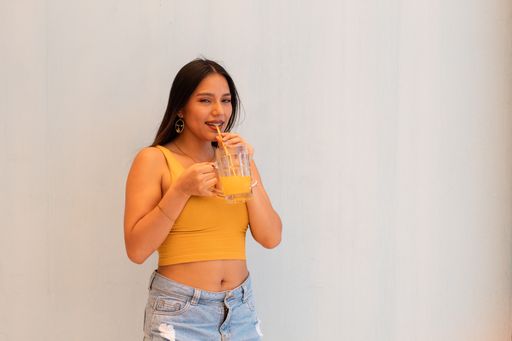 A hispanic girl wearing orange top drinking juice and looking at camera