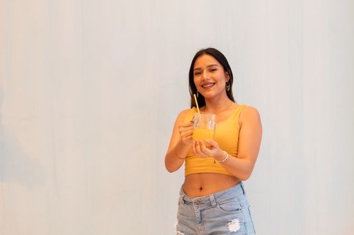 A hispanic girl wearing orange top holding glass of juice and looking at camera