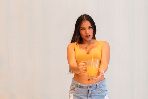 A hispanic girl wearing orange top holding glass of juice and looking at camera