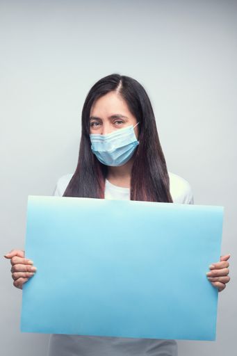 A young female doctor in a medical mask holding a blank board-COVID-19