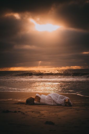 A vertical shot of a female posing at a beach during the sunset