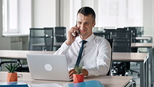 A Caucasian business man sitting in his office and talking on phone with laptop in front of him