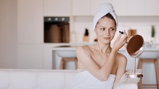 A beautiful Caucasian young lady putting makeup in front of mirror and sitting on white sofa