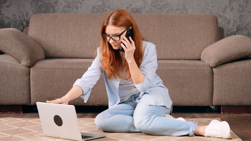 A beautiful Caucasian girl sitting on ground and talking on phone while using laptop