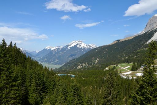 A high angle shot of a beautiful mountain range covered with green fir trees and snow under the cloudy sky
