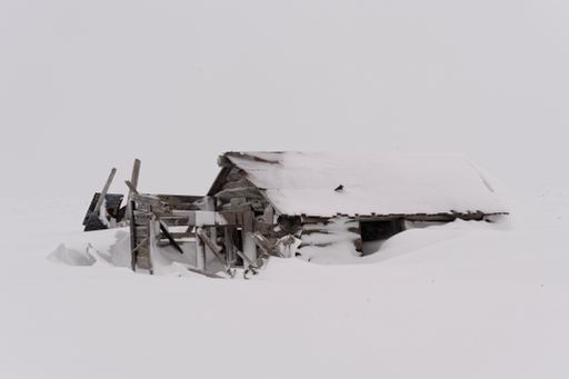 Desolate log cabin covered in drifting snow along Bering sea coast in Alaska