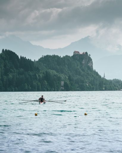A back view of a person kayaking in the lake with castle and mountains in the background