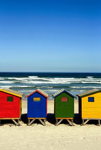 A vertical shot of vibrant, colorful little beach huts with a lovely view of the calm sea under a clear sky on a sunny day