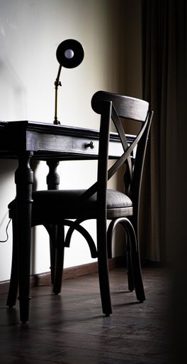 A vertical shot of a wooden chair and a table with a lamp on it
