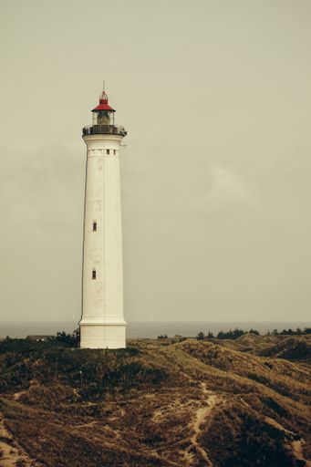 A vertical shot of a white lighthouse against a gray cloudy sky