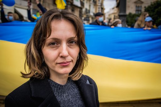 Ukrainian Refugee at Demonstration Against War with Russia Looking Optimistically at Camera with Giant National Flag in Background
