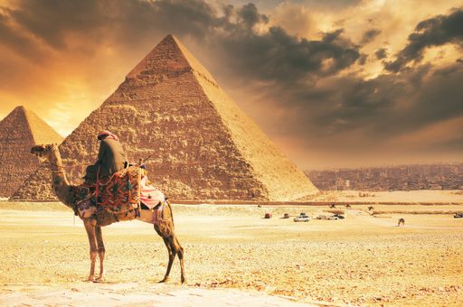 A scenic view of a person on a camel with the Pyramids in the background in Egypt