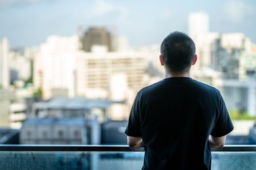 The back of a male watching the city from high rise building balcony