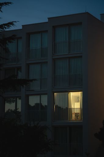 A vertical shot of a modern white building with light coming out from one of the big balcony windows