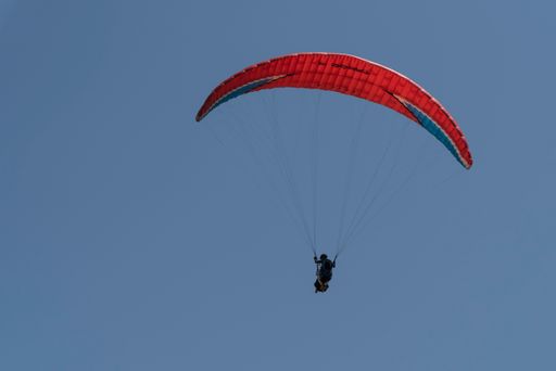A low angle shot of a paraglider flying in the clear blue sky with a red parachute