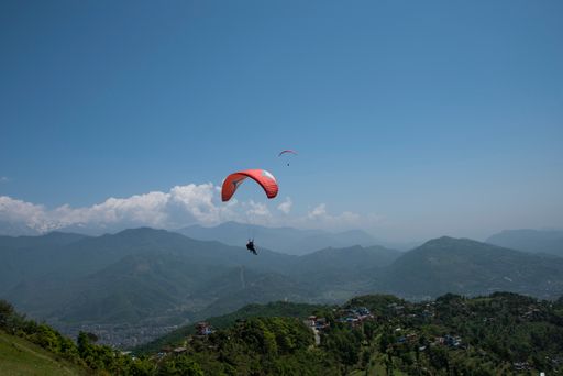 An aerial shot of a paraglider floating in the sky above the lush greenery from Sarangkot to Pokhara