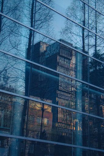 A vertical shot of the blue glass building wall reflecting other buildings.