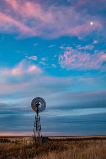 A vertical shot of a windpump against a blue cloudy sky during the sunset
