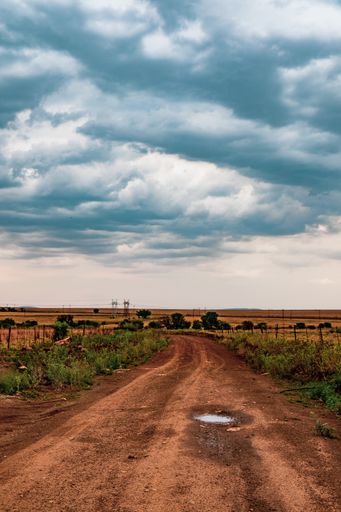 A vertical shot of an empty sand road under a cloudy sky