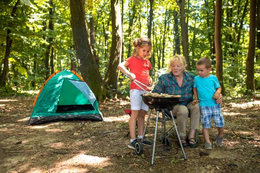 A closeup of kids with their grandma having fun while making a barbecue in a forest