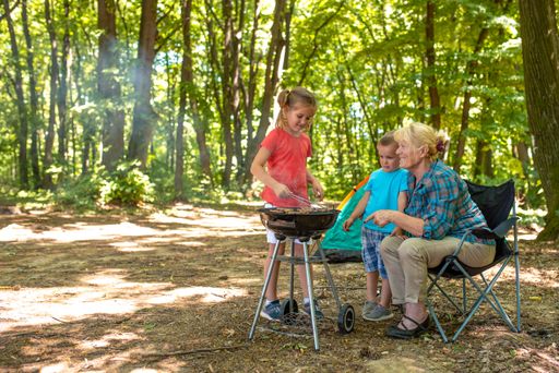A closeup of kids with their grandma having fun while making a barbecue in a forest