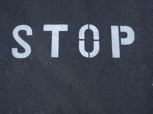 White stop sign painted on dark asphalt. You can see tire tracks over it. Indicates a mandatory stop.
