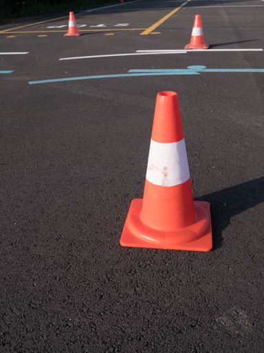 A closeup shot of traffic cone with white and orange stripes on gray asphalt, copy space