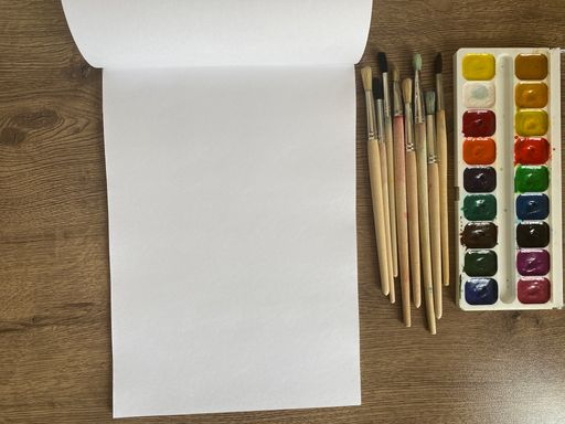 A set of different paint brushes with watercolor paints and white album pages