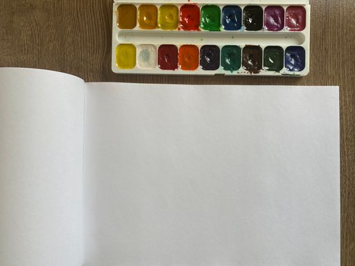 The watercolor paints with white album pages on a wooden table