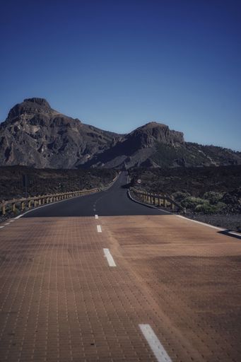 A vertical shot of a highway road with white signs and mountains in a distance