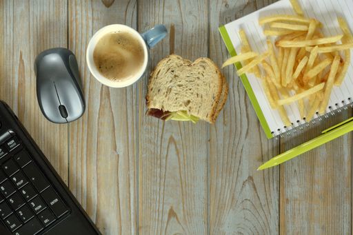 A wireless mouse, fried potatoes, cup of coffee, piece of bread and notebook with pen isolated on a wooden surface - work at home concept