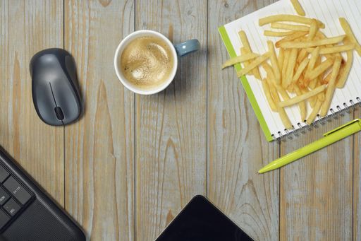 A wireless mouse, fried potatoes, cup of coffee and notebook with pen isolated on a wooden surface - work at home concept