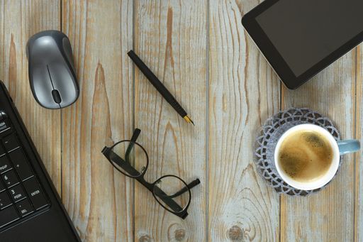 A wireless mouse, a cup of coffee, tablet and optical eyeglasses isolated on a wooden surface - work at home concept