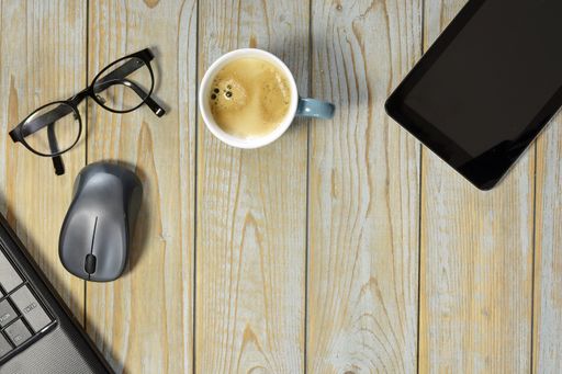 A wireless mouse, a cup of coffee, tablet and optical eyeglasses isolated on a wooden surface - work at home concept