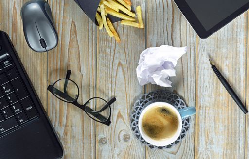 A wireless mouse, a cup of coffee, fried potatoes, tablet and optical eyeglasses isolated on a wooden surface - work at home concept