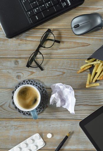 A wireless mouse, a cup of coffee, fried potatoes, tablet, pills and optical eyeglasses isolated on a wooden surface - work at home concept