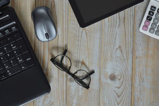 A laptop, digital tablet with a wireless mouse, optical eyeglasses and calculator isolated on a wooden surface - work at home concept